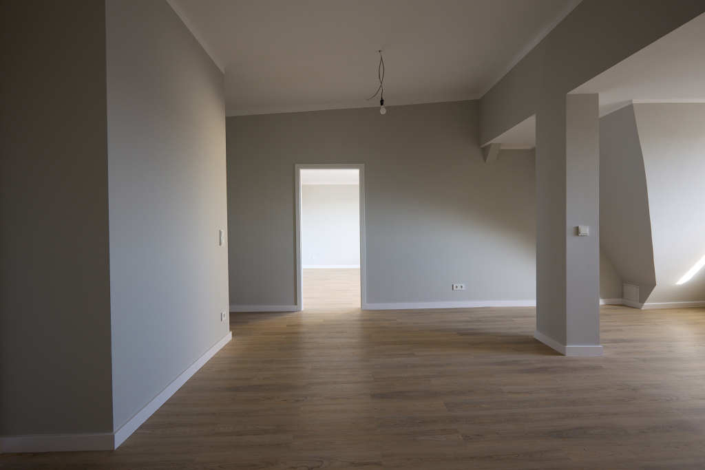 Raw photograph of an empty apartment with laminate flooring, angular architectural elements and harsh highlights.