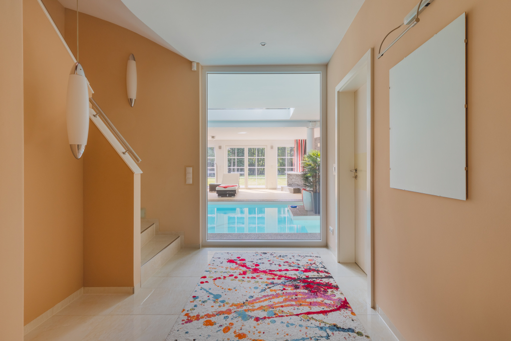 Ground level hallway next to half-turn staircase and suspended chandeliers, leading to the indoor pool of a villa.