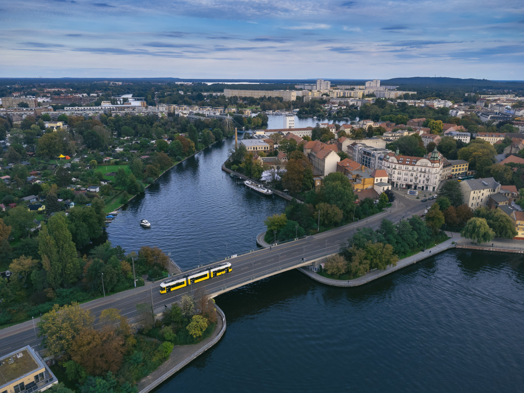 Drohnenaufnahme einer BVG-Straßenbahn über die Dammbrücke, die die Spree und Müggelspree trennt.