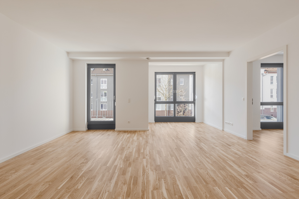 Empty rooms with white walls, laminate flooring, window walls and a balcony accessed through a glass double glazed door.