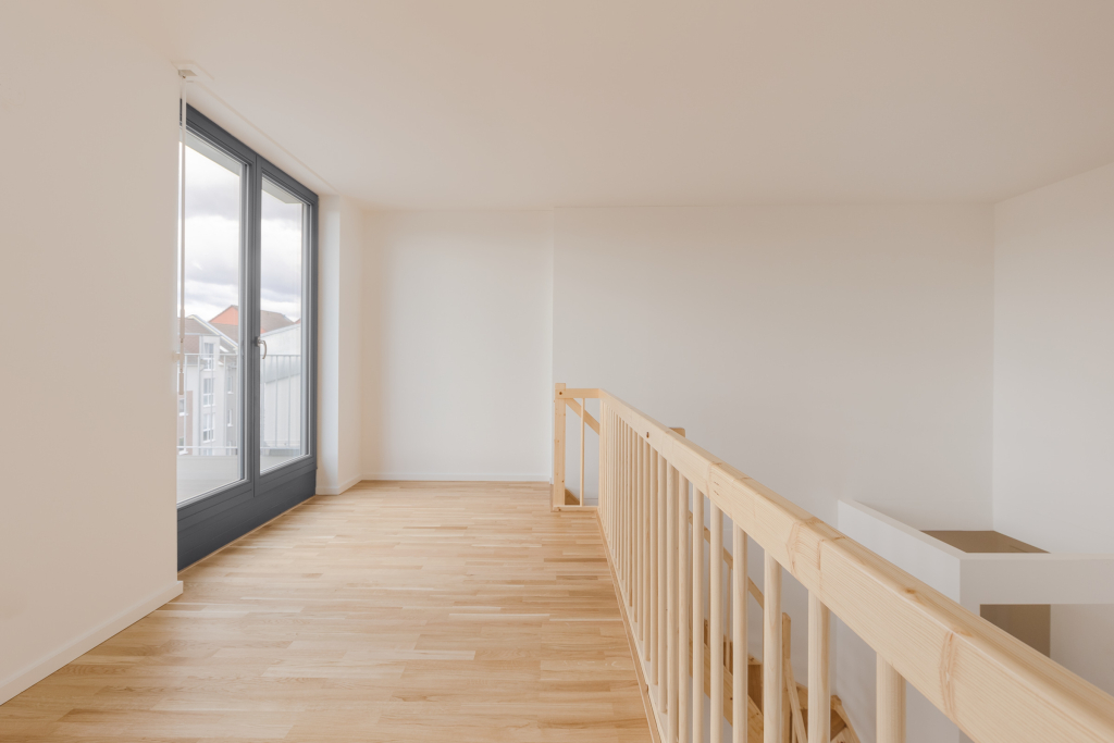 View of the second floor of a small loft suite with wooden staircase, white walls and a balcony.