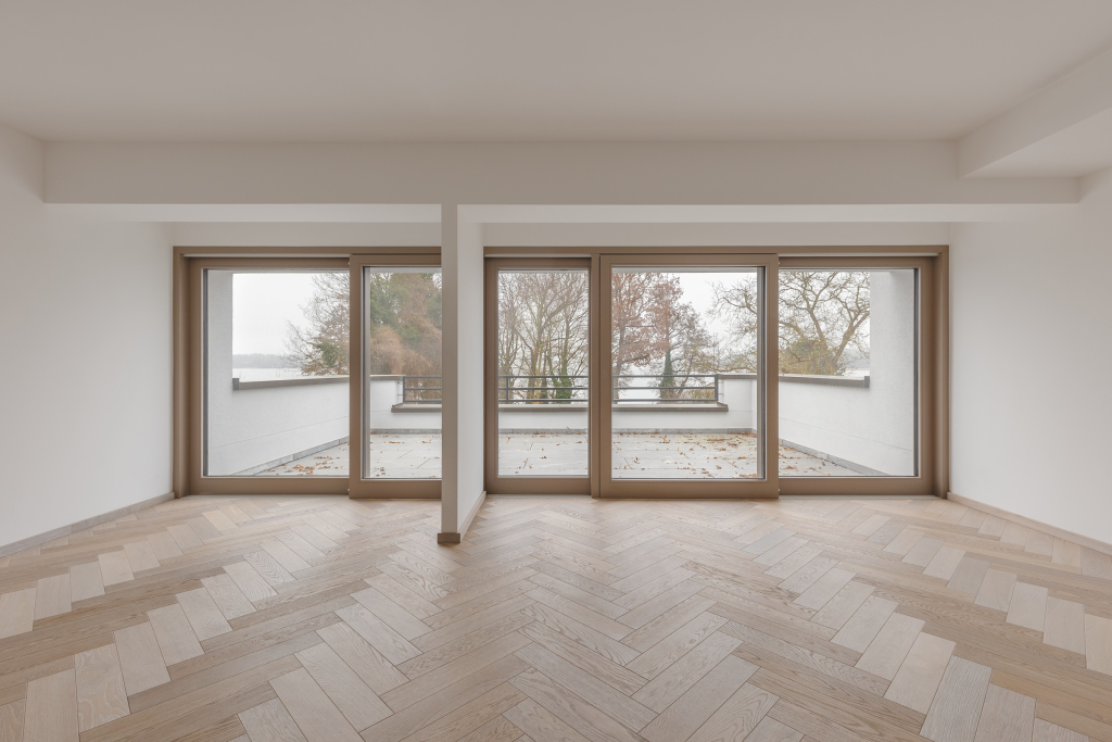 Close-up of the transition between an empty room with big windows and a large open balcony through glass sliding doors.