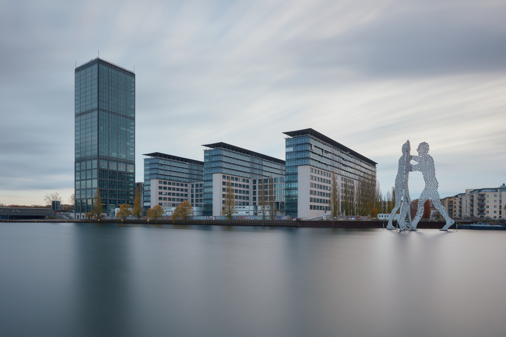 Long exposure photograph of the Treptower office building and Molecule Man sculpture on the Spree river in Berlin.