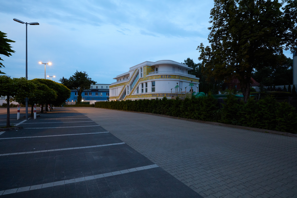 Blick über einen Parkplatz auf einen Kindergarten am frühen Abend in Grünau, Berlin. Testbild mit hohem Rauschen mit einer Canon 5DS R bei ISO 3200.