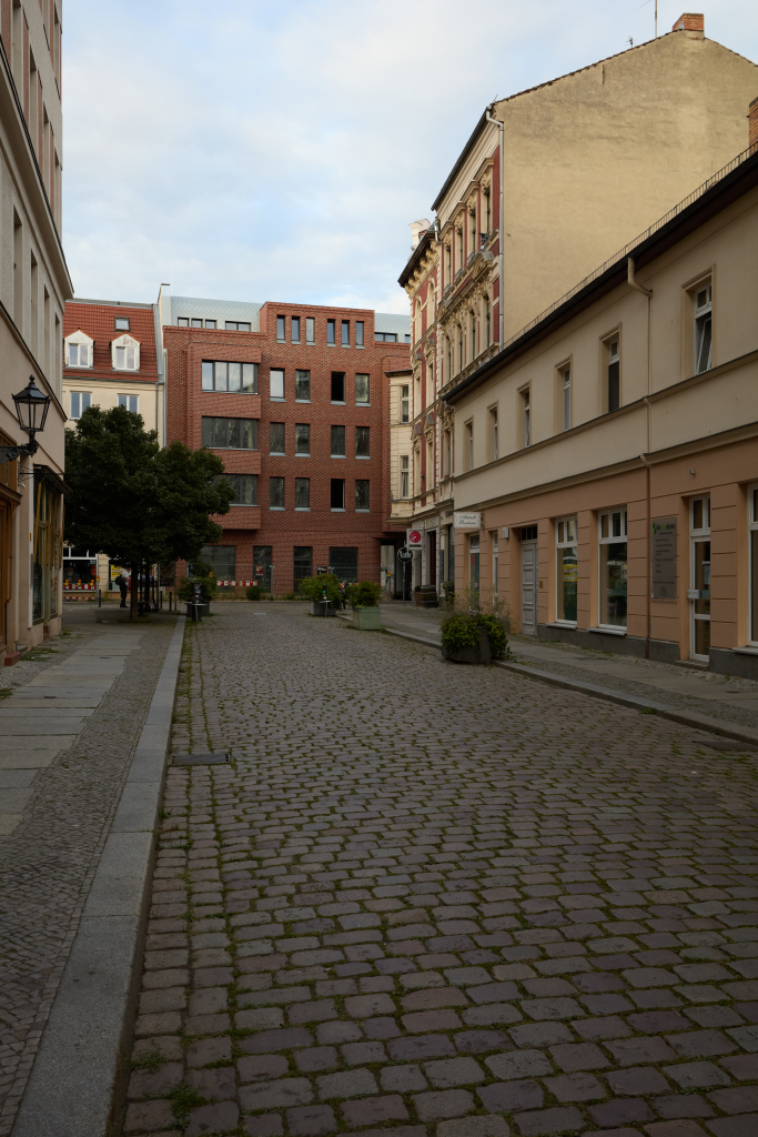 Eine ruhige Stadtstraße mit historischen Gebäuden und einem neu errichteten Gebäude am Ende, aufgenommen am frühen Abend in Köpenick, Berlin.