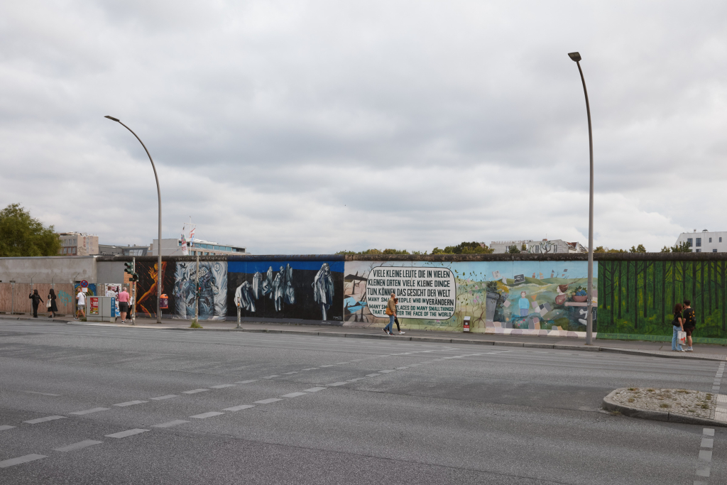 Overview at an intersection of the East Side Gallery, Berlin, featuring murals by Ana L. M. Rodrigues, Kani Alavi, Muriel Raoux and Ditmar Reiter.