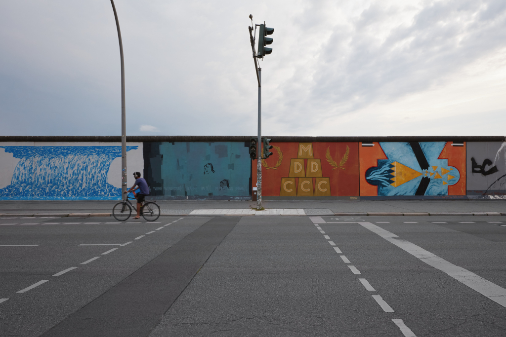 Cyclist in front of the East Side Gallery, Berlin, with murals by Imre Gábor, Pál Gerber, Gábor Gerhes and Sándor Györffy in the background.