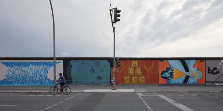 Radfahrer vor einem Teil der East Side Gallery in Berlin bei Sonnenuntergang.