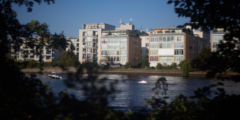 A riverside view of modern apartment buildings, framed by trees and captured with a vintage Helios lens, creating a soft, nostalgic atmosphere.