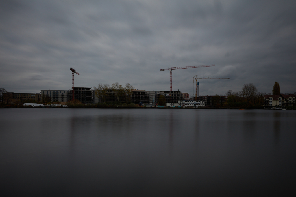 Long exposure shot of the construction site along the river, slightly brighter than the first, revealing faint details amidst the shadows.