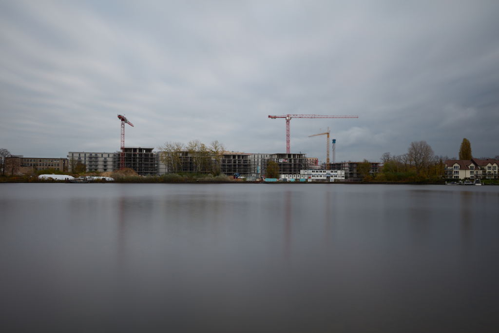 Well-balanced long exposure image of the construction site, capturing clear details of machinery and soft cloud movement against the overcast sky.