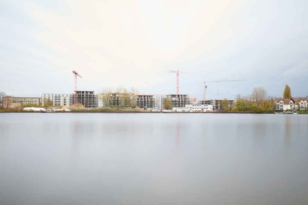 Overexposed long exposure image of a construction site across the river, where bright highlights have washed out the details of the structures.