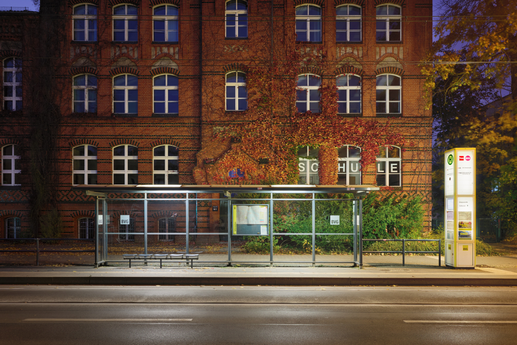 BVG tramway station in front of a school taken at night, near Grünau, Berlin. Autumn leaves and cool lighting add contrast to the warm tones of the scene.