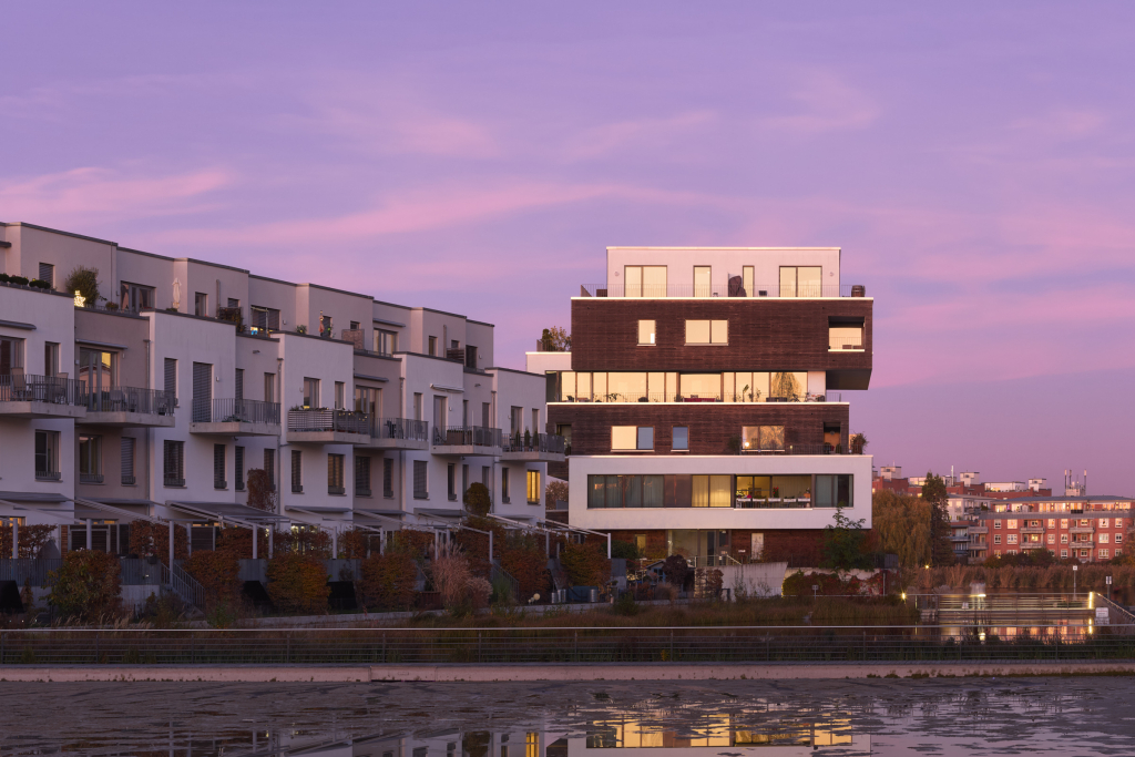 Modern apartments at dusk with sleek design. A purple sky casts a serene glow over the scene. Located on the Dahme river near Grünau, Berlin.