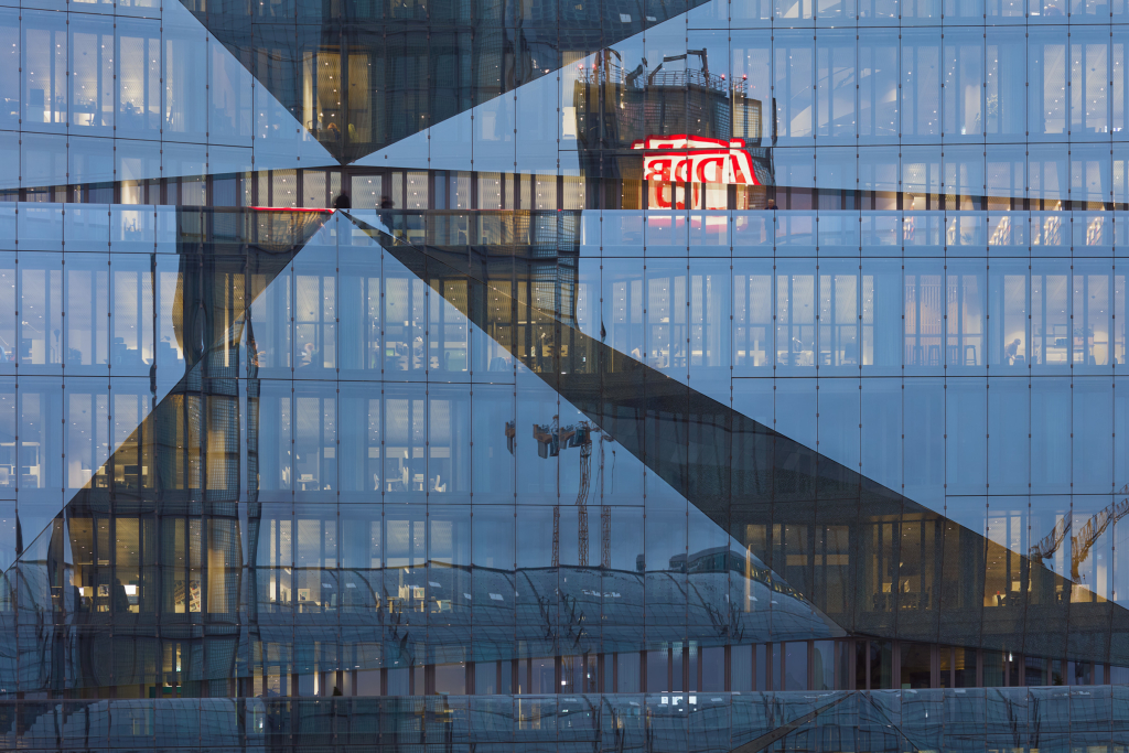 Der Berliner Hauptbahnhof spiegelt sich während der blauen Stunde im Gebäude des 3XN Cube Berlin.