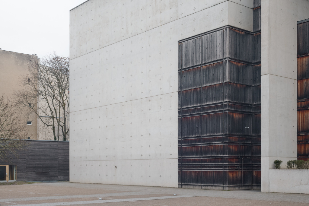 Detailansicht des Eingangs der St.-Canisius-Kirche, wobei das Zusammenspiel der Texturen von Sichtholz und Beton mit Kreuzmustern im Vordergrund steht.