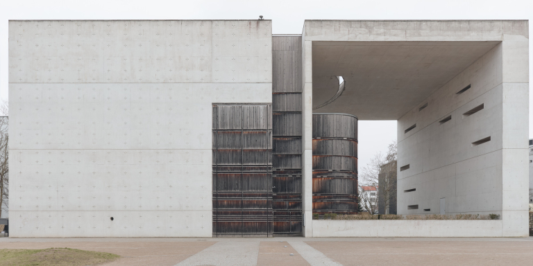 Anterior view of St. Canisius Church, Berlin - brutalist concrete with rusted wood panels and geometric openings on an overcast day.