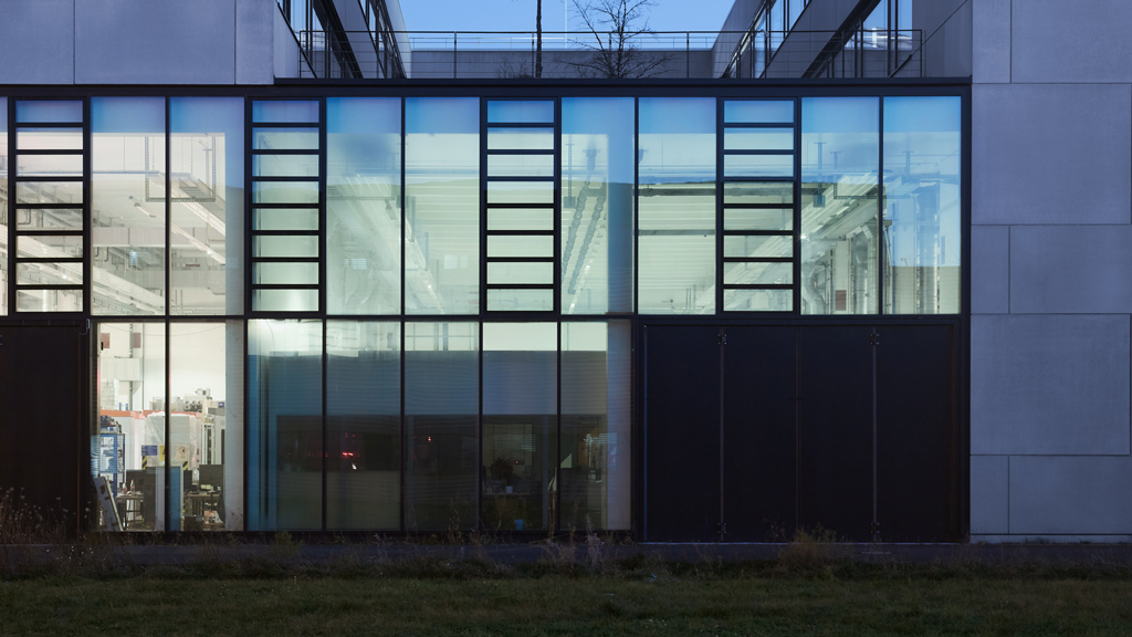 Rear perspective of an industrial building with large windows lit from within at twilight in Adlershof, Berlin.