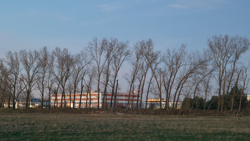Industrial buildings and storage facility partially obscured by trees in Adlershof, Berlin.