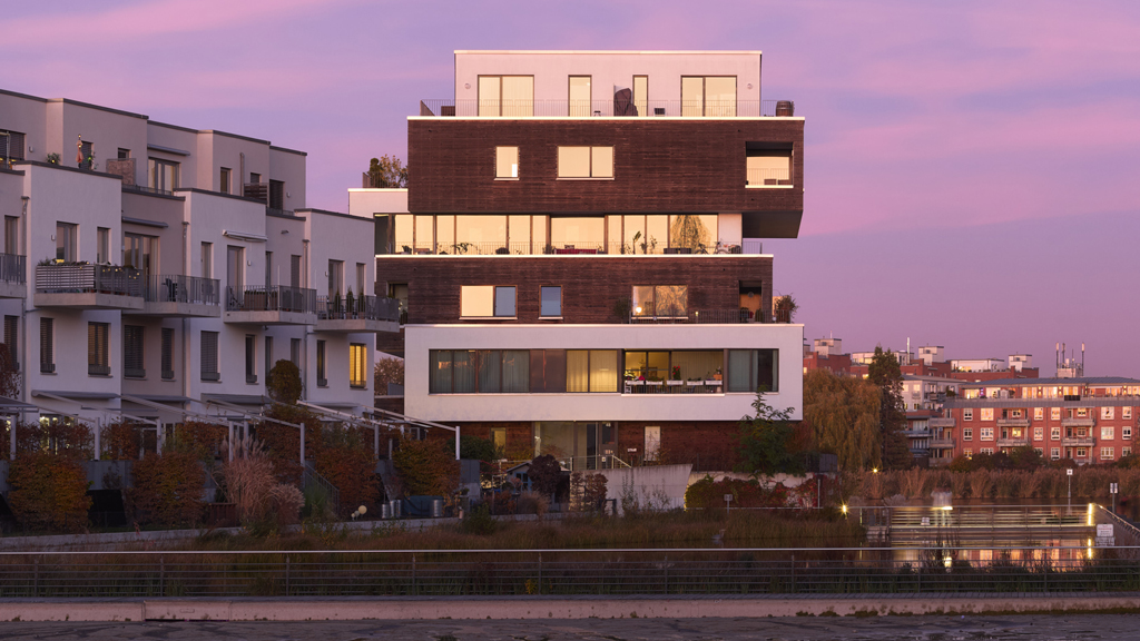 Modern riverside apartments near Grünau, Berlin, under a tranquil purple dusk sky.