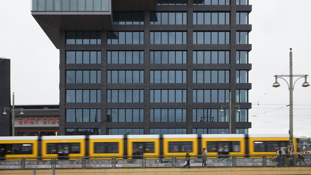 Urban scene showing a BVG tram passing in front of the Edge East Side Tower near Warschauer Straße, Berlin.