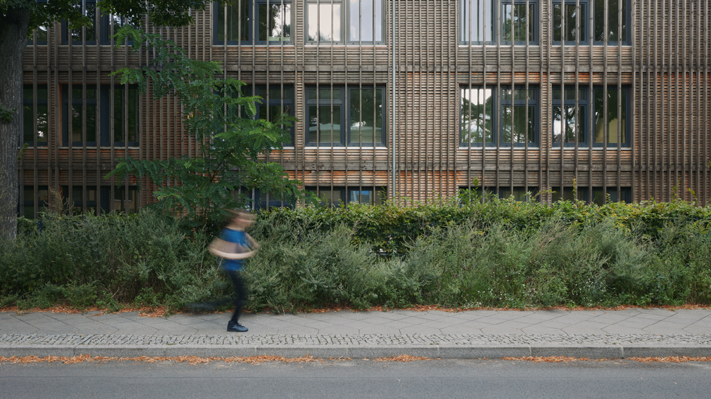 Runner in motion in front of a kindergarten featuring wood-clad architecture in Spindlersfeld, Berlin.