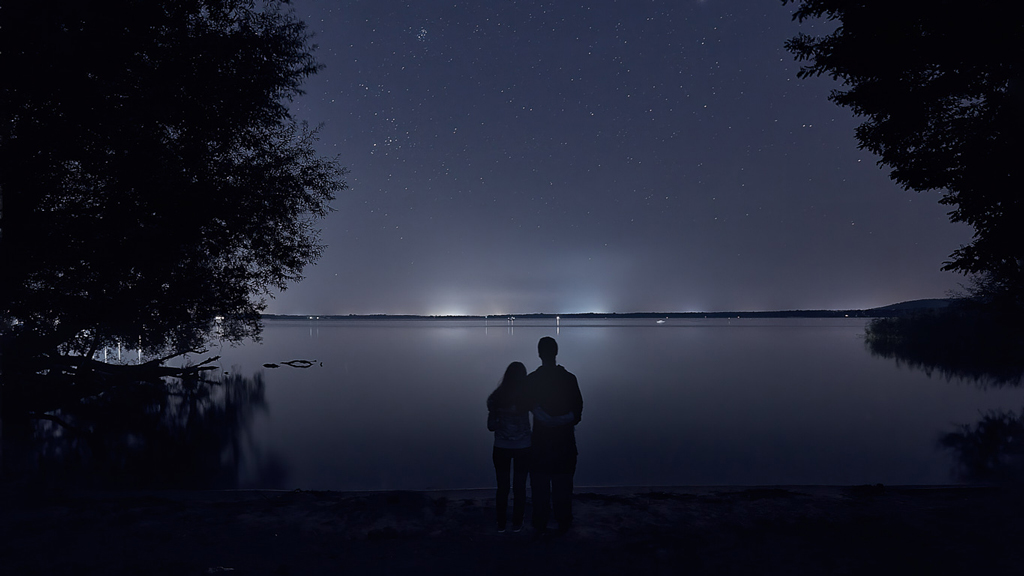 Couple silhouetted against the starry night sky overlooking Großer Müggelsee in a long exposure.
